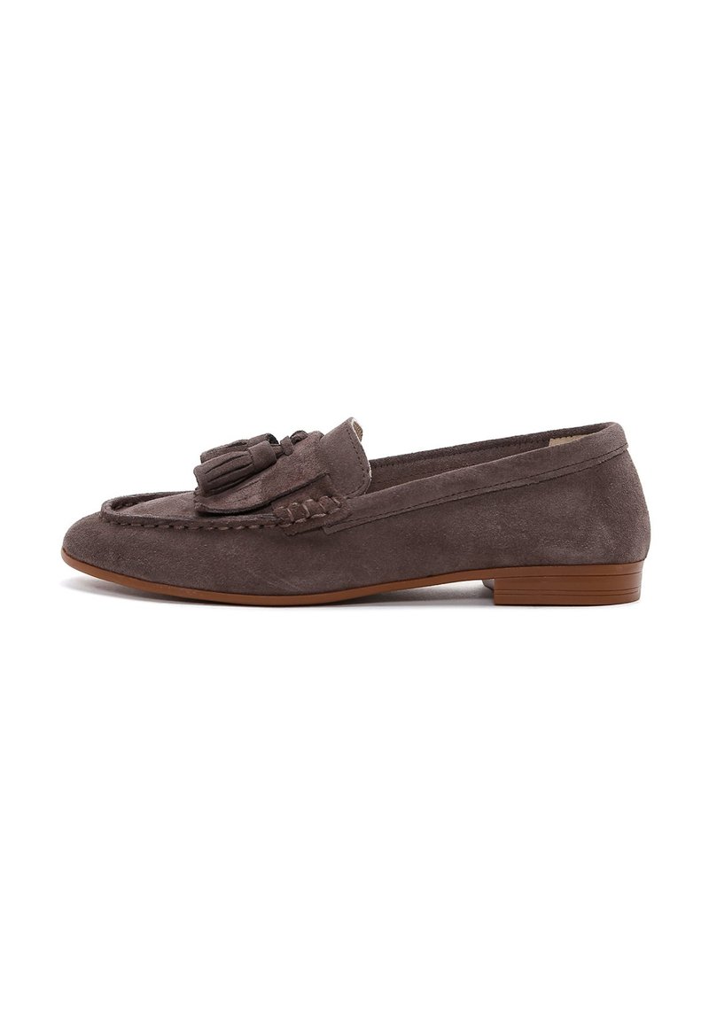 Mocassin en daim gris avec un petit talon, présentant des détails de glands sur le devant et des surpiqûres décoratives sur les bords. Texture lisse sur l'ensemble.
