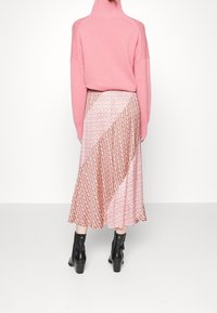 Hellrosa Oversize-Pullover kombiniert mit einem gemusterten, diagonal geteilten Rock in Pink- und Rottönen. Schwarze Knöchelstiefel runden den Look ab.