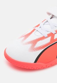 Zapatilla deportiva blanca con acentos rojos, que presenta una parte superior de malla transpirable, un patrón texturizado y una suela de goma con detalles de agarre.