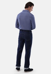 Camicia azzurro chiaro, testurizzata, con colletto; abbinata a jeans in denim scuro, con risvolti, e scarpe in suede nere. Vista posteriore dell'outfit.