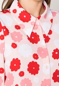 Blommig skjortblus med rosa bakgrund, med stora röda och vita blommönster, spridd krage och lätt, mjuk tyg.