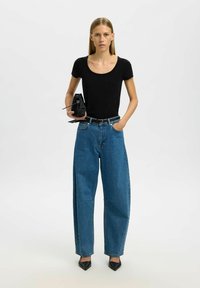 Sort scoop-neck t-shirt, løse blå denim jeans med høj talje og spidse sorte hæle; holder en lille sort taske.