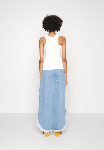 White sleeveless top, loose light blue jeans with fringed hem, and orange block-heeled sandals. Textured fabric with a soft finish.