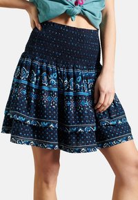 Blå och svart mönstrad kjol med ett smockat midjeband, utsvängd design och lager av volanger med blommönster och polka prickar.