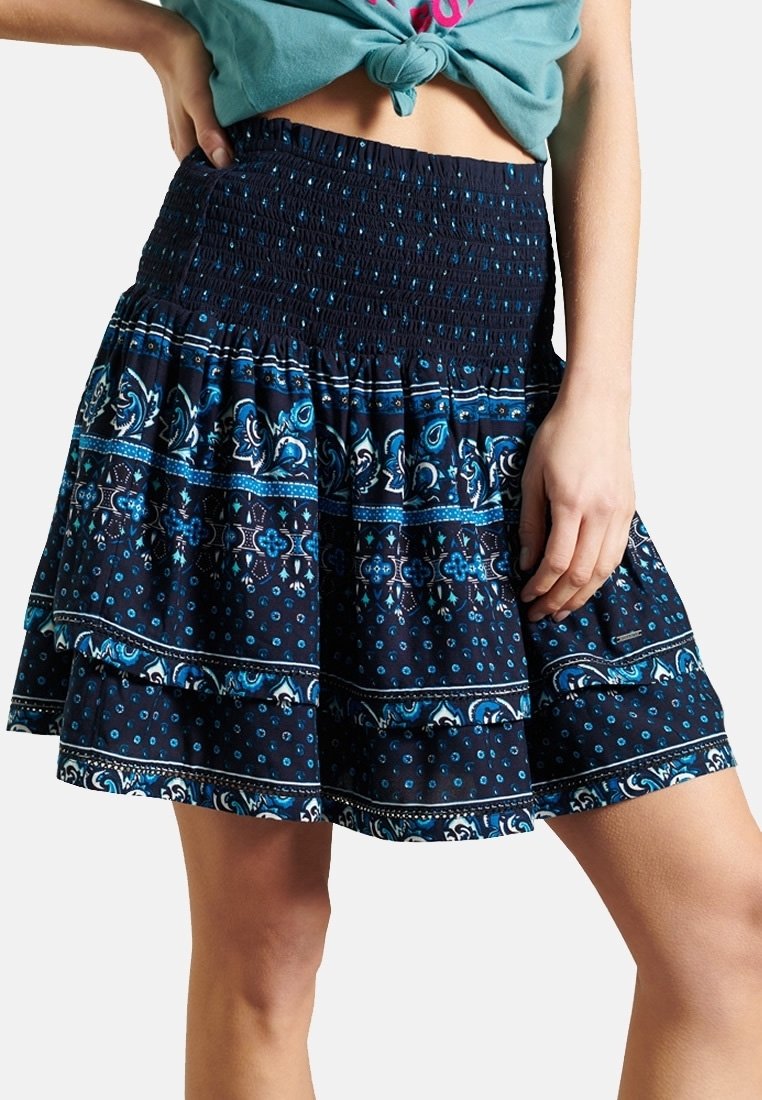 Blå och svart mönstrad kjol med ett smockat midjeband, utsvängd design och lager av volanger med blommönster och polka prickar.