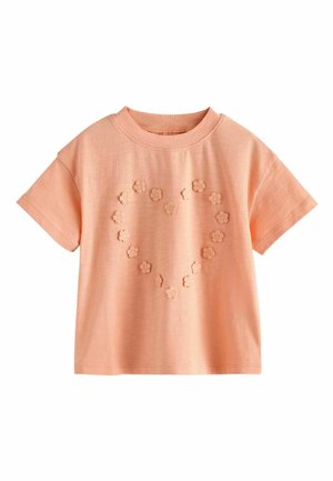 Peach-colored short-sleeve cotton shirt with round neckline and heart-shaped pattern of small raised fabric flowers on front.