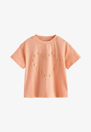 Virspõll pehme puuvillane lühikeste varrukatega pluus virsikuvärvi, ümar kaelus ja ees südameläheline muster väikestest ülestõstetud kangast lillekestest.