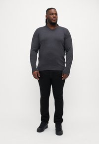 Maglione grigio scuro a scollo a V abbinato a jeans neri slim-fit e sneaker nere. Il tessuto appare morbido con una consistenza liscia.