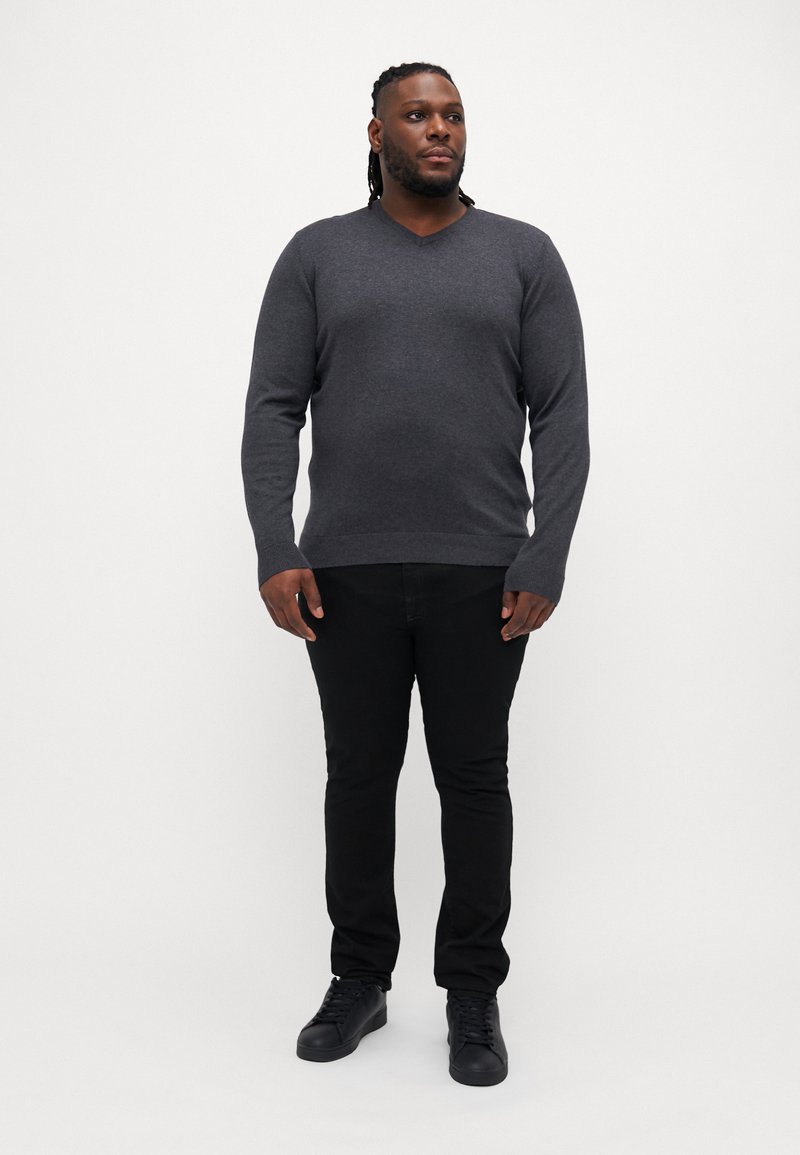 Suéter gris oscuro de cuello en v combinado con jeans negros ajustados y zapatillas negras. La tela parece suave con una textura lisa.