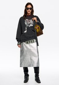 Melnā kapuce ar grafiku, kārtota virs šūnveida krekla, apvienota ar metālisku sudraba svārku un melniem augstiem zābakiem.