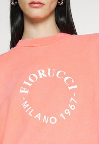 Koraalroze sweatshirt van katoen, met een rond wit logo met de tekst "Fiorucci" en "Milano 1967", en ribboorden bij de hals en mouwen.
