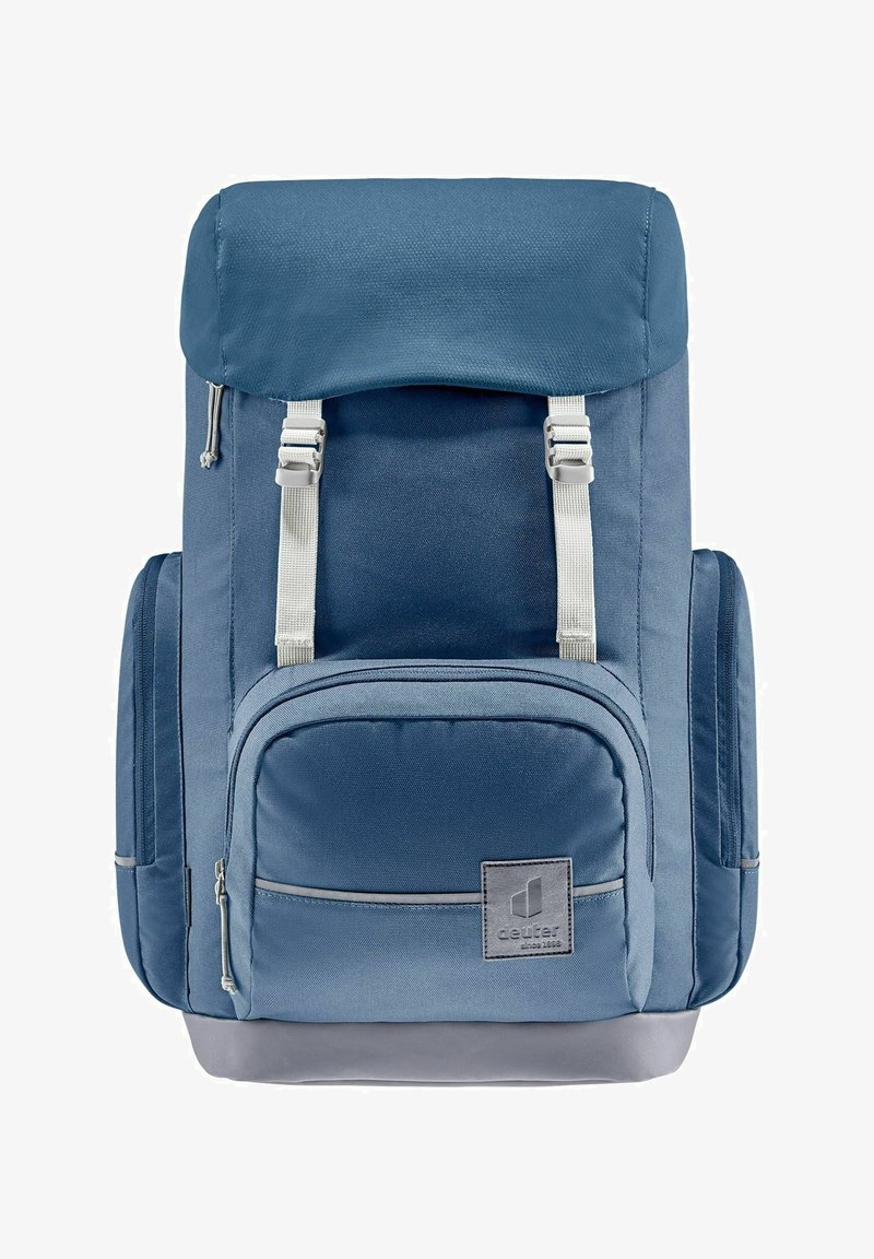 Mochila de tela azul con cierre enrollable, correas gris claro, un bolsillo frontal con cremallera y base gris. Presenta un material texturizado y un parche con el logo.