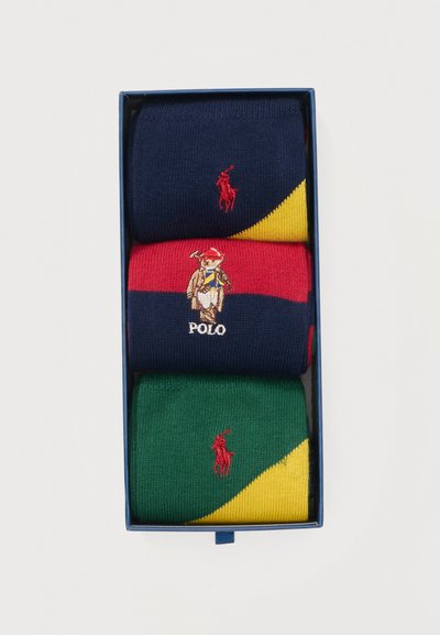 Τρία ζευγάρια διπλωμένα καλτσάκια Polo σε μπλε κουτί, με χρώματα ναυτικού μπλε, κόκκινου και πράσινου, με κίτρινες λεπτομέρειες και κεντημένα λογότυπα.