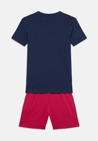 Κοντομάνικο μπλε μπλουζάκι με στρογγυλή λαιμόκοψη και κόκκινο σορτς. Και τα δύο είναι κατασκευασμένα από απαλό βαμβάκι, με λεία υφή και χωρίς εμφανή σχέδια.