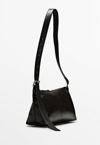Borsa a tracolla in pelle nera con finitura liscia, cuciture sottili, tracolla regolabile e chiusura con zip. Forma compatta e triangolare.