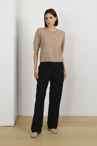 Beige kortærmet strikket sweater med tekstureret overflade, parret med sorte brede bukser og beige udsmykkede flade sko, mod en neutral baggrund.