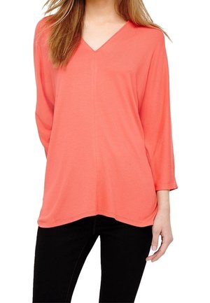 T-shirt corail en tissu léger, avec des manches trois-quarts et une coupe décontractée, associé à un pantalon noir.