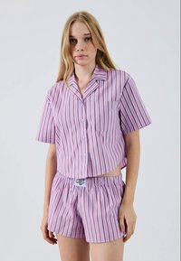 Ensemble de pyjama à manches courtes rayé en violet clair et rose, comprenant un haut à boutons avec une poche et un short à taille élastique. Tissu doux.