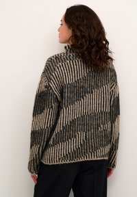 Overmaat gebreide trui in beige en zwart. Kenmerkt zich door verticale en diagonale gestreepte patronen met een textuur, geweven stof. Hoge halslijn.