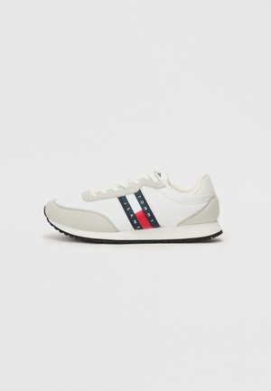 Scarpe da corsa da uomo con corpo in tessuto bianco, dettagli in suede grigio, suola in gomma nera e un design del logo a strisce rosse e blu.