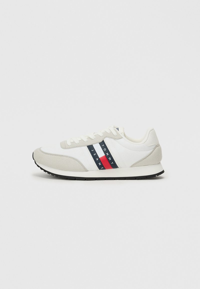 Męskie buty do biegania z białym materiałowym korpusem, szarymi zamszowymi akcentami, czarną gumową podeszwą oraz czerwoną i niebieską paskową grafiką logo.