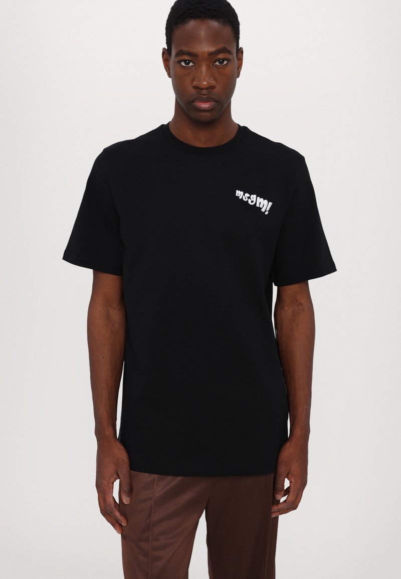 Camiseta de algodón negra con cuello redondo y mangas cortas. Un texto blanco decorativo en el pecho añade detalle. Diseño simple y limpio.
