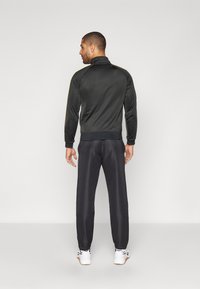 Black sports jacket with a high collar and ribbed cuffs, paired with black track pants, both in a smooth, lightweight material.