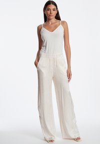 Witte mouwloze top met V-hals, gecombineerd met wijde, crèmekleurige textuurbroek. De broek heeft een elastische tailleband en zijzakken.