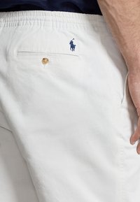 Bílé bavlněné šortky s elastickým pasem, zapínací zadní kapsou a vyšitým námořnickým logem polo na pravé straně.