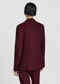 Blazer bordeaux a righe con revers, chiusura a bottone singolo e maniche lunghe. Presenta doppi spacchi posteriori e quattro bottoni decorativi sulle maniche.