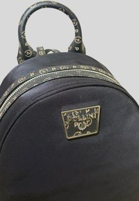 Zaino in tessuto nero con forma circolare, zip dorata e piastra con logo distintivo. Manico superiore con dettagli decorati.