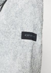 Giacca grigia chiaro morbida e pelosa, realizzata in materiale soffice, con una superficie strutturata e un'etichetta nera con la scritta "ICEMARKO" sulla manica superiore.