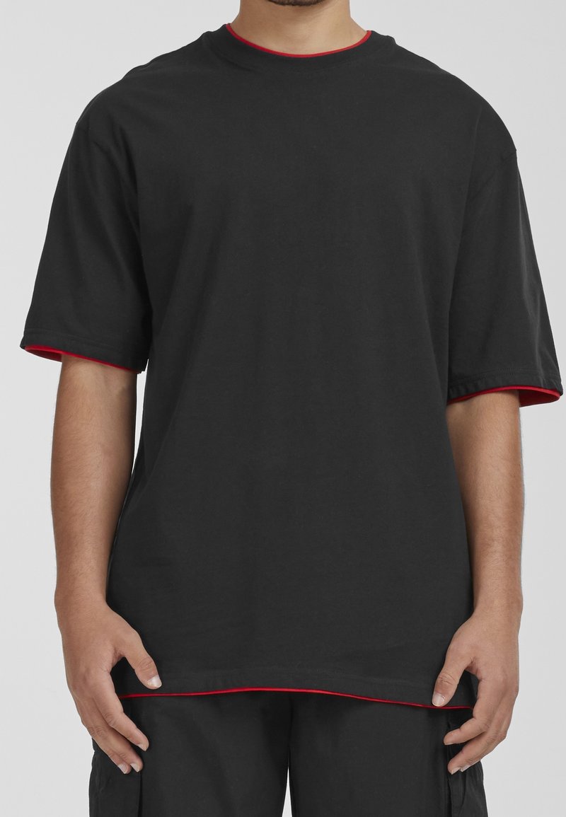 Schwarzes kurzärmeliges T-Shirt aus Baumwolle, mit roten Akzenten am Kragen und an den Ärmelsäumen. Reguläre Passform mit geradem Schnitt.