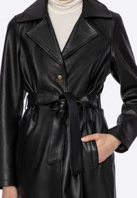Černý kožený kabát s výstřihovým límcem, zapínáním na jedno tlačítko, páskem v pase a bočními kapsami, s hladkou a měkkou texturou.