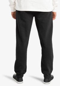 Black sweatpants made of soft fabric, featuring a relaxed fit, elastic cuffs, and side pockets. Worn with casual black sneakers.