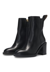 Botas de cuero negro hasta el tobillo con punta afilada, cremallera lateral y tacón grueso. Textura suave con un ligero brillo y diseño minimalista.