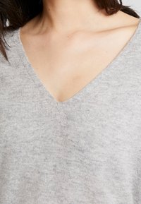 Hellgrauer V-Ausschnitt-Pullover aus einem weichen Strickmaterial, mit einem entspannten Design und einer subtilen Textur ohne sichtbare Muster oder Akzente.