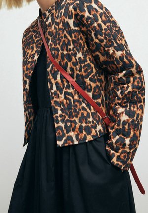 Personne portant une veste à imprimé léopard sur une robe noire avec une sangle rouge de sac bandoulière visible sur la poitrine et l'épaule.