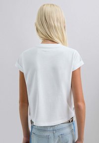 Witte katoenen cropped t-shirt met opgerolde korte mouwen, met een subtiele logo-afdruk op de achterkant nabij de halslijn.