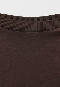 Brauner Baumwollstoff mit einem strukturierten, gerippten Bund und einem glatten Körper. Das Material wirkt weich und flexibel.