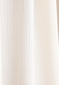 Tessuto leggero e plissettato in un delicato bianco sporco con righe verticali. La trama appare liscia e leggermente traslucida.