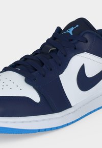 Χαμηλού τύπου αθλητικό παπούτσι με δέρμα σε ναυτικό μπλε και λευκό, μπλε κορδόνια, μπλε λογότυπο Nike Swoosh και ανοιχτό μπλε λογότυπο Jumpman στη γλώσσα.