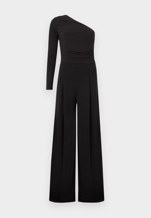 Must ühe õlaga kombinesoon vasaku pika varrukaga, kitsaskohaga ja laiade säärega pükstega, neutraalse tausta ees.