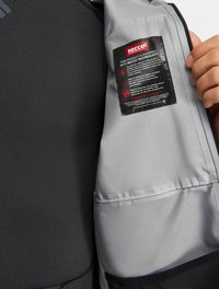Wnętrze szarej kurtki z etykieta technologii RECCO, o gładkiej teksturze i przeszywanych szwach. Widoczna jest czarna zewnętrzna tkanina.