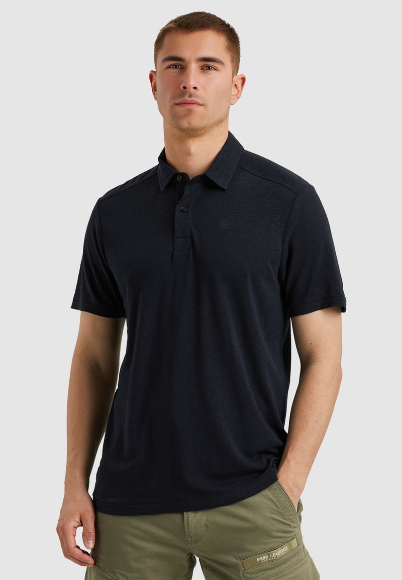 Marineblauwe polo met korte mouwen, voorzien van een klassieke kraag, een twee-knoopsluiting en een subtiele logodetail op de borst. Gemaakt van zachte stof.