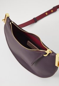 Purple leather handbag with a textured finish, gold zipper, and hardware accents. Interior features a contrasting red lining.