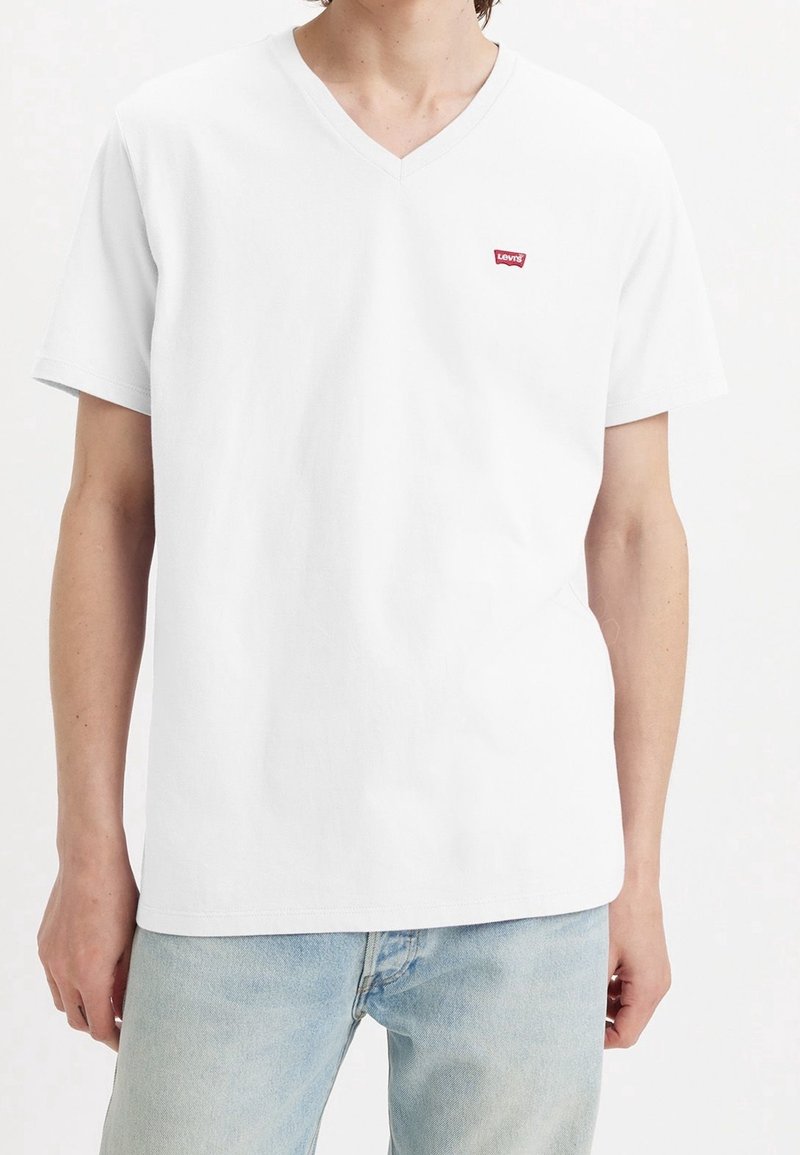 T-shirt V-cou à manches courtes en coton blanc avec un petit patch logo rouge Levi's sur la poitrine gauche. Texture douce, coupe décontractée.