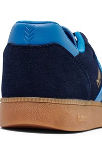 Navy suede sneaker with blue accents and a textured gum sole. Features a smooth heel tab with raised design and detailed stitching.