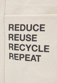 Tissu en toile avec un texte noir audacieux sur une poche indiquant "RÉDUIRE RÉUTILISER RECYCLER RÉPÉTER" promouvant des actions durables.