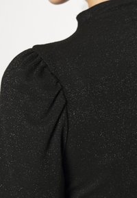 Top in tessuto nero con filo glitterato, maniche a sbuffo gatherate e collo alto, che presenta una superficie liscia e accenti luccicanti.